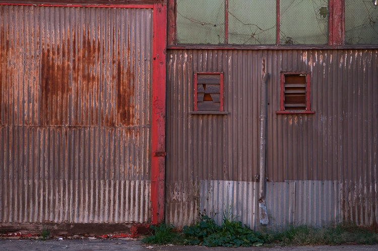 A rusty shed door with peeling red paint