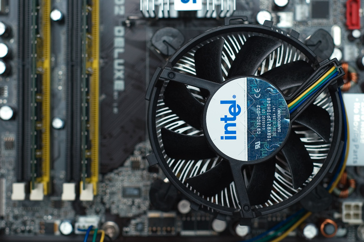 Closeup of a CPU cooler (fan and heatsink) with a motherboard in the background