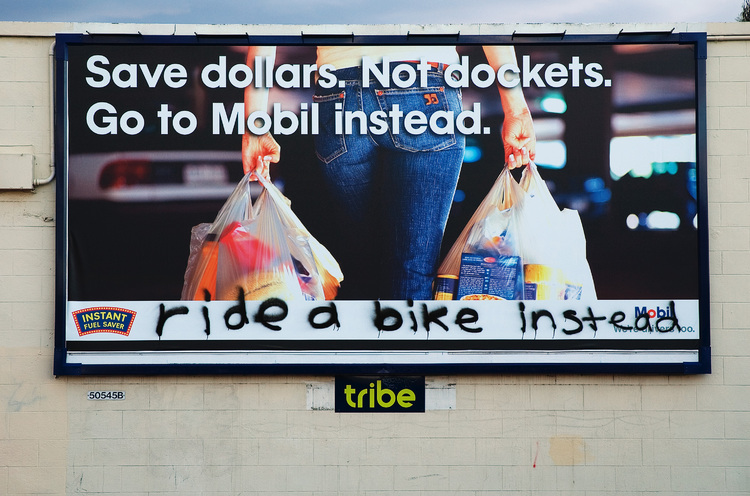 'ride a bike instead' graffitied across a billboard