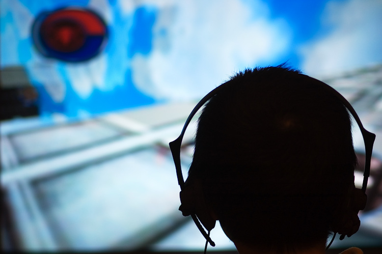 The silhouette of a head (wearing headphones), against a a TV screen