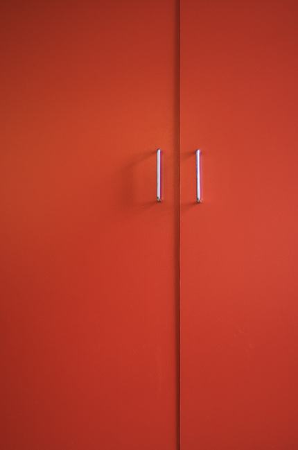 A pair of cupboard door handles on orange doors