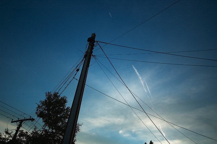 Jet contrails in the dusk sky, seen past a mess of wires