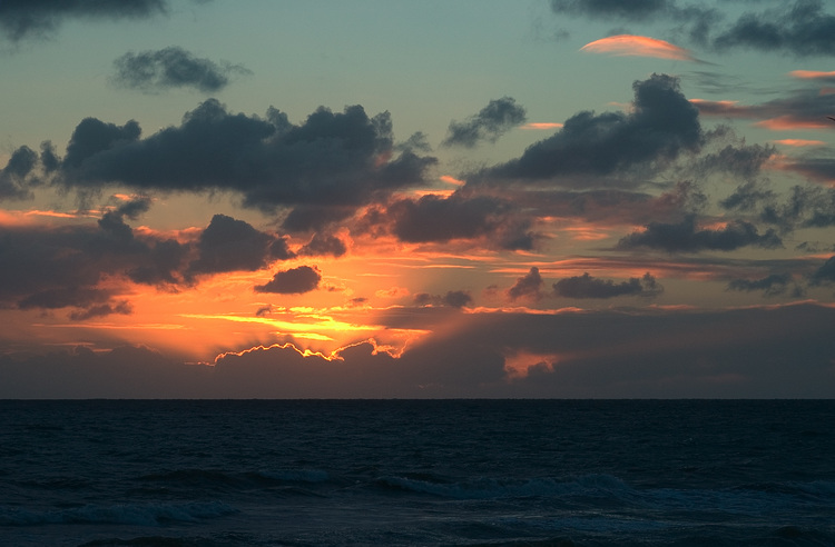 The sun setting over the sea (behind clouds)