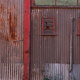 A rusty shed door with peeling red paint