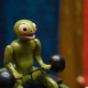 Interactive sculpture of a little green guy lifting weights