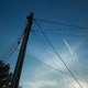 Jet contrails in the dusk sky, seen past a mess of wires